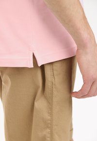 Ljusrosa bomullspolo med delad nederkant, tillsammans med beiga bomullsshorts med sidsömmar. Fokusera på textil- och färgdetaljer.