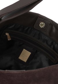 Unutrašnjost smešnog kožnog tašnice od smešnog zamka ima zippered džep, zlatni hardver i suptilni logotip uzorak na crnoj tkanini obloge.