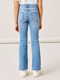 Jeans acampanados de color azul claro con una cintura alta, que presentan dos bolsillos traseros y un borde rematado. Combinados con zapatillas blancas.