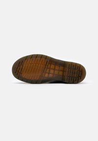 Semelle de chaussure avec bande de roulement en caoutchouc marron transparent montrant un motif en grille et des zones de grip texturées sur fond blanc.
