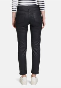 Černé kalhoty z umělé kůže se slim fit střihem, vybavené dvěma zadními kapsami a hladkým povrchem. V kombinaci s bílými teniskami.