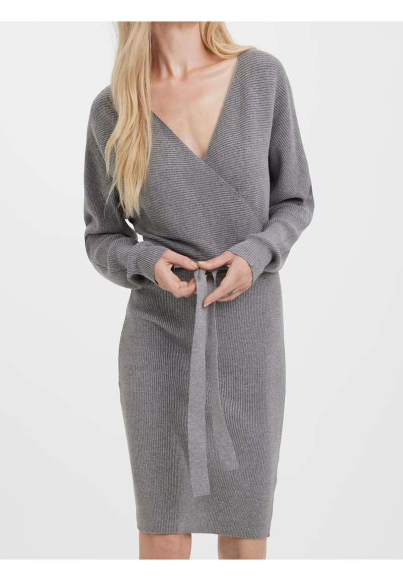 Femme attachant une ceinture à la taille sur une robe portefeuille gris en maille côtelée à manches longues et décolleté en V.