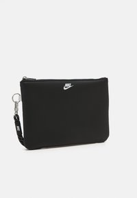 Crna Nike torbica s glatkom teksturom, pravokutnog oblika, zatvaranjem na patentni zatvarač i istaknutim bijelim logotipom na prednjoj strani. Ima odvojivu trakicu.
