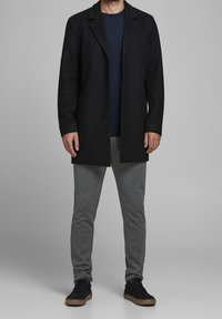 Černý vlněný kabát s klopami, zapínání na jeden knoflík, šedé tepláky a černé tenisky s hnědou podrážkou. Jednoduchý a moderní design.