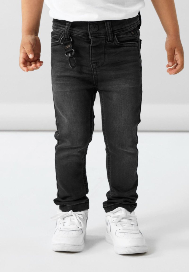 Musta farkut slim fit -mallilla, joissa on etutaskusuunnittelu ja vyölenkki. Yhdistetty valkoisiin lenkkareihin.
