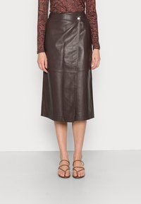 Gonna midi in pelle marrone con un design elegante, caratterizzata da una chiusura laterale a pressione, cuciture piatte e una texture liscia.