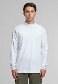 Camiseta de manga larga blanca con un cuello alto, hecha de algodón suave. Presenta un corte relajado y no tiene patrones ni diseños visibles.