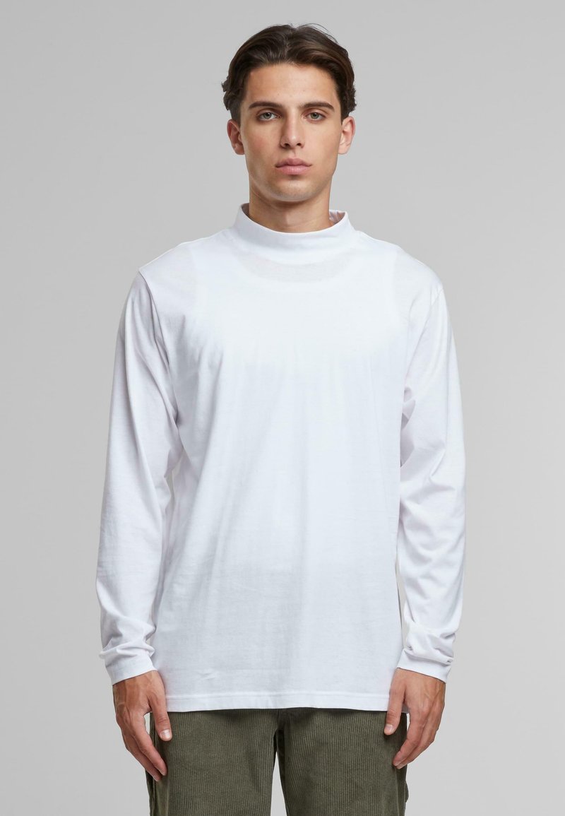 Camiseta de manga larga blanca con un cuello alto, hecha de algodón suave. Presenta un corte relajado y no tiene patrones ni diseños visibles.
