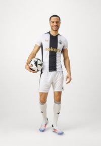Completo da calcio maschile con una maglia a strisce bianche e navy, con dettagli neri, logo e testo dorato, abbinata a pantaloni corti bianchi e calze al ginocchio.