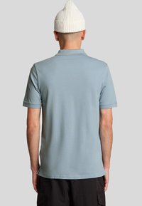Polo shirt in lichtblauwe stof, korte mouwen en een rechte zoom. Heeft een ribgebreide kraag en rug met een plat gebreid ontwerp.