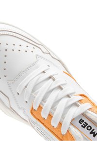 White leather sneaker with orange suede accents, featuring perforated detailing, white laces, and a textured sole.