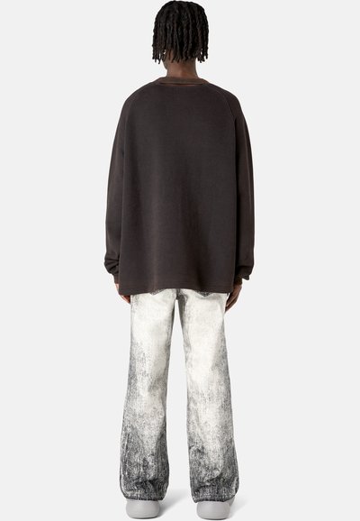 Übergroßer dunkelgrauer Sweatshirt, kombiniert mit ausgefransten hellgrauen und schwarzen Schlagjeans, die eine strukturierte Oberfläche und eine lässige Passform haben.