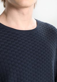 Marinblå stickad tröja med struktur, rundad halsringning och rutmönster, med en mjuk, vävd finish.