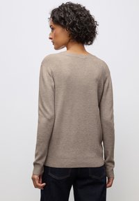 Beige gestrickter Pullover mit langen Ärmeln und rundem Ausschnitt. Gerippte Textur, an den Handgelenken eng anliegend, kombiniert mit dunkelblauen Jeans.