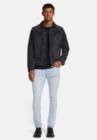 Svart denimjacka med två bröstfickor och knäppning, i kombination med en svart skjorta, ljusblå jeans och svarta skor.