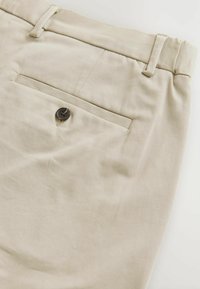Beige Baumwollhose mit einer Gesäßtasche mit einem dunklen Knopf, flachem Schnitt und subtiler Textur.