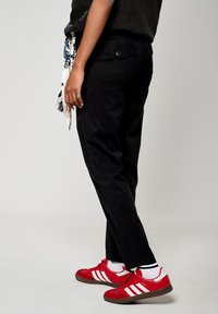 Pantalones negros con un corte relajado, tejido texturizado y bolsillos laterales; combinados con zapatillas rojas con rayas blancas y una suela negra.
