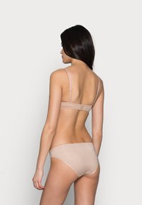Beige lingerie set met een beha met dunne verstelbare bandjes en haaksluiting, gecombineerd met een bijpassende slip, beide van gladde stof.
