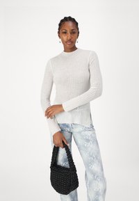 Lys grå ribbet langermet topp kombinert med teksturerte lys blå slangeskinsjeans, holder en liten svart vevd håndveske.