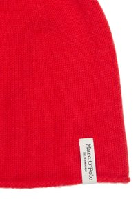 Rode gebreide beanie van zachte wol. Heeft een opgevouwen rand met een wit label waarop 'Marc O'Polo' in zwarte tekst staat. Gestructureerd oppervlak.