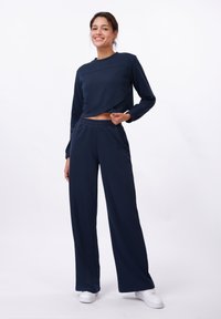 Haut court à manches longues bleu marine avec un col rond, associé à un pantalon large. Fabriqué en tissu doux, avec une taille élastique.
