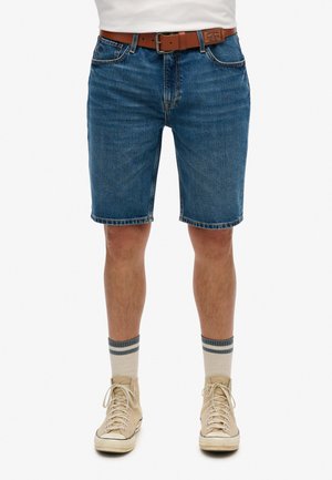 Shorts en denim bleu moyen avec une coupe droite, cinq poches et une ceinture en cuir marron. Complétés par des baskets montantes beiges et des chaussettes rayées.