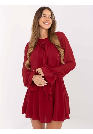 Czerwona sukienka z długim rękawem o rozkloszowanym kroju, z drapowanym wzorem i kwiatowym akcentem przy dekolcie. Lekka, zwiewna tkanina.