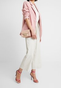 Donna che indossa un blazer rosa, pantaloni a gamba larga bianchi a righe, sandali con tacco rosa, e porta una piccola borsa a spalla rosa.