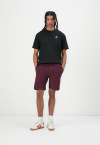 Svart t-shirt med liten logotyp, vinröda shorts med dragsko i midjan och krämfärgade sneakers med röda ränder. En enkel och avslappnad outfit.