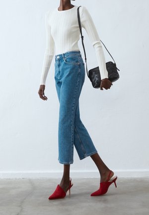 Maglia bianca a costine a manica lunga, jeans blu a gamba dritta, mules rosse con punta a punta e borsa a tracolla nera intrecciata.