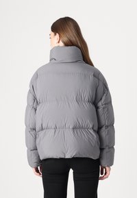 Grå pufferjakke med høj krave, quiltet tekstur og et afslappet snit. Har lange ærmer og et cropped design.
