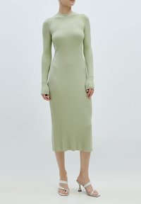 Robe à manches longues en maille côtes vert clair, silhouette ajustée, col rond, tricot texturé. Portée avec des talons blancs ouverts, design minimaliste.