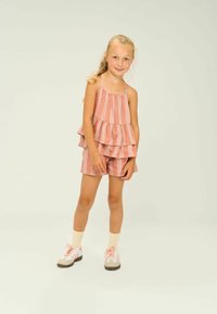 Rózsaszín és fehér csíkos, rétegezett ujja nélküli felső, hozzá illő sorttal. Az öltözet lágy anyagból készült, laza fazonú, sportcipővel párosítva.
