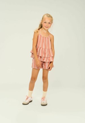 Randig topp i rosa och vitt med lager och utan ärmar, tillsammans med matchande shorts. Kläderna har ett mjukt material och en avslappnad passform, ihop med sneakers.