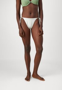 Zeleni bikini zgornji del z žico, v kombinaciji z belimi bikini hlačkami z nizkim pasom, ki imajo bočne vezi. Gladka tekstura in minimalističen dizajn.