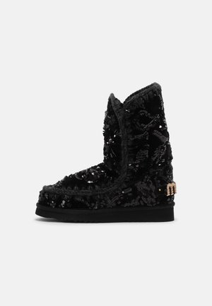 Mustad mustad mustad, kaetud sädelevate kummikutega, millel on tekstuuriga äär ja külgedel kuldse tooni logo aktsent. Lame tallaga disain.