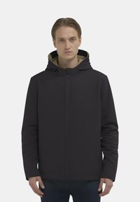 Giacca nera con chiusura a zip e cappuccio, caratterizzata da una trama liscia e tasche laterali inclinate. L'interno è di colore beige, visibile al colletto.