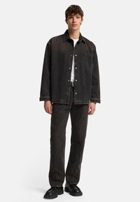 Camicia di jeans nera e pantaloni abbinati, con una vestibilità comoda, chiusura a bottoni, tasca frontale e tessuto testurizzato. Scarpe nere completano l'outfit.