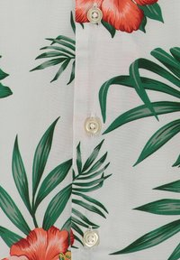 Weißer Stoff mit einem tropischen Muster aus grünen Palmblättern und orangen Hibiskusblüten, mit drei weißen Knöpfen entlang der Mitte.