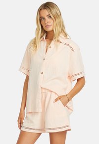 Set di camicia e pantaloni corti rosa chiaro, tessuto testurizzato, chiusura anteriore con bottoni, maniche corte, dettagli decorativi a intaglio lungo gli orli e le spalle.