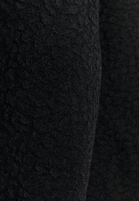 Černá texturovaná tkanina s jemným vyvýšeným vzorem, která má měkký, mírně lesklý povrch a hladký finiš.