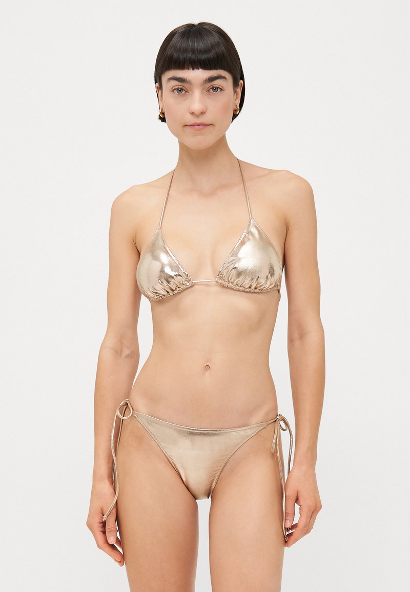 Bikini metallico oro con coppe triangolari e lacci regolabili, abbinato a slip a vita bassa con lacci laterali. Texture liscia e lucentezza.