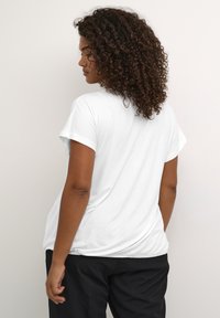 Vit kortärmad t-shirt med rundad halsringning och rynkad nederkant, tillsammans med mörka byxor. Mjuk tyg med en slät yta.