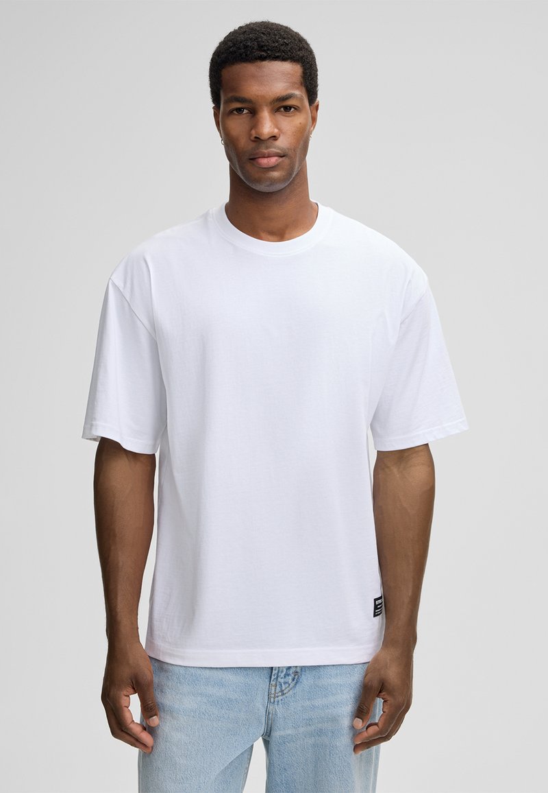 Weißes Baumwoll-T-Shirt mit kurzen Ärmeln und rundem Ausschnitt. Verfügt über eine lockere Passform und ein kleines Markenlabel in der Nähe des Saums.