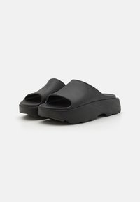 Sorte plattform sandaler i sort laget av gummi, med åpen tå og bred, buet rem. Teksturert såle for grep.