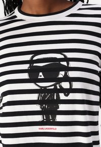 Svart og hvit stripete t-skjorte laget av bomull, med grafikk av en karakter med solbriller. "KARL LAGERFELD" trykt i rødt.
