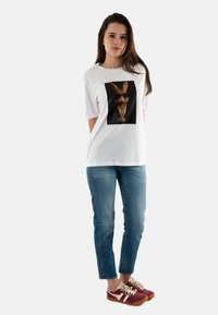 Camiseta blanca con un gráfico central de un conejo estilizado con gafas de sol. Combínala con unos vaqueros azules y zapatillas burdeos con detalles en blanco.