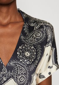 Blusa a maniche corte con un motivo paisley blu navy e crema, dotata di colletto e scollatura a V profonda. Texture satinata liscia.
