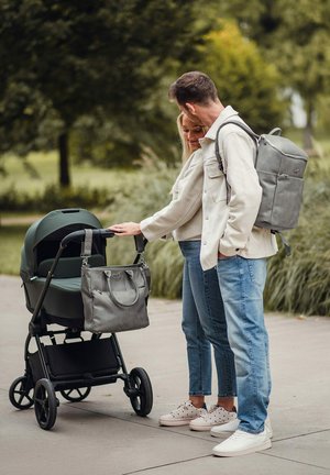 Kočárek v tmavě zelené látce s černým rámem, doplněný o šedou texturovanou tašku na pleny. Pár si povídá vedle kočárku.