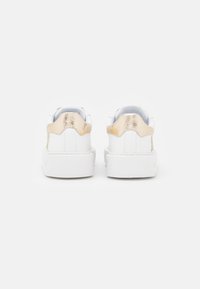 Valkoiset tennarit, joissa on sileä nahkapinta, metallinhohtoinen kultainen kantapääkappale ja pehmustettu nilkkakaulus. Yksinkertainen, tyylikäs muotoilu.